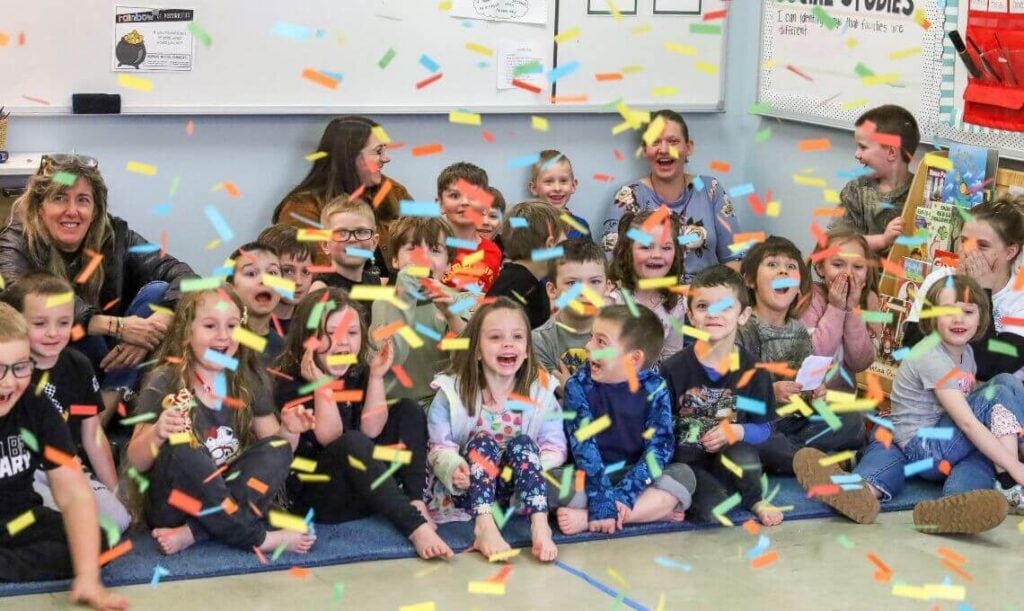 preschool children sit on a gum mat in a classroom with confetti flying down