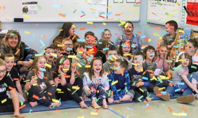 preschool children sit on a gum mat in a classroom with confetti flying down