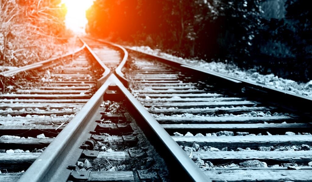 close up of two railroad tracks diverging with sunlight streaming low on them