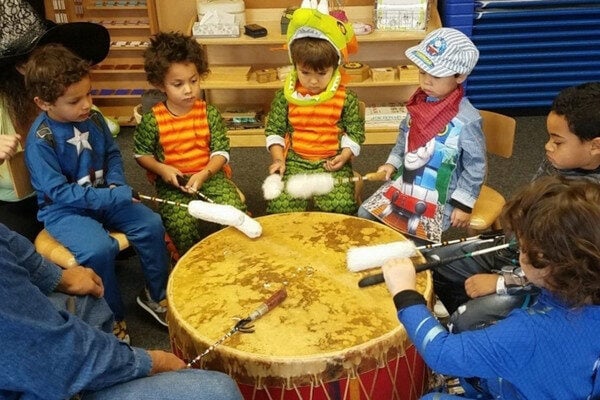 young children in costumes sit around a large drum learning how to play