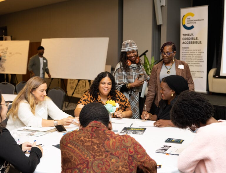 A group of people sitting and standing around a round table at a policy conference