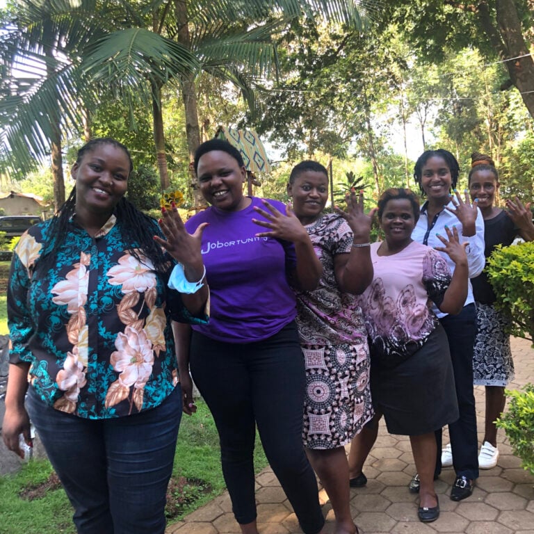 Six black women in Tanzania hold up five fingers to signal a job opportunity program.